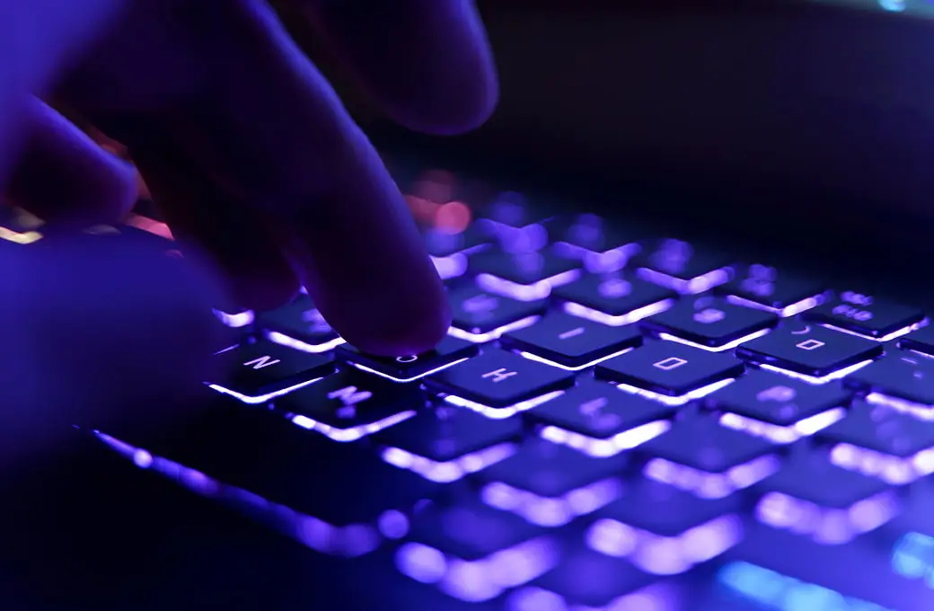 青い光のバックライトに照らされたキーボードを指で操作している様子。